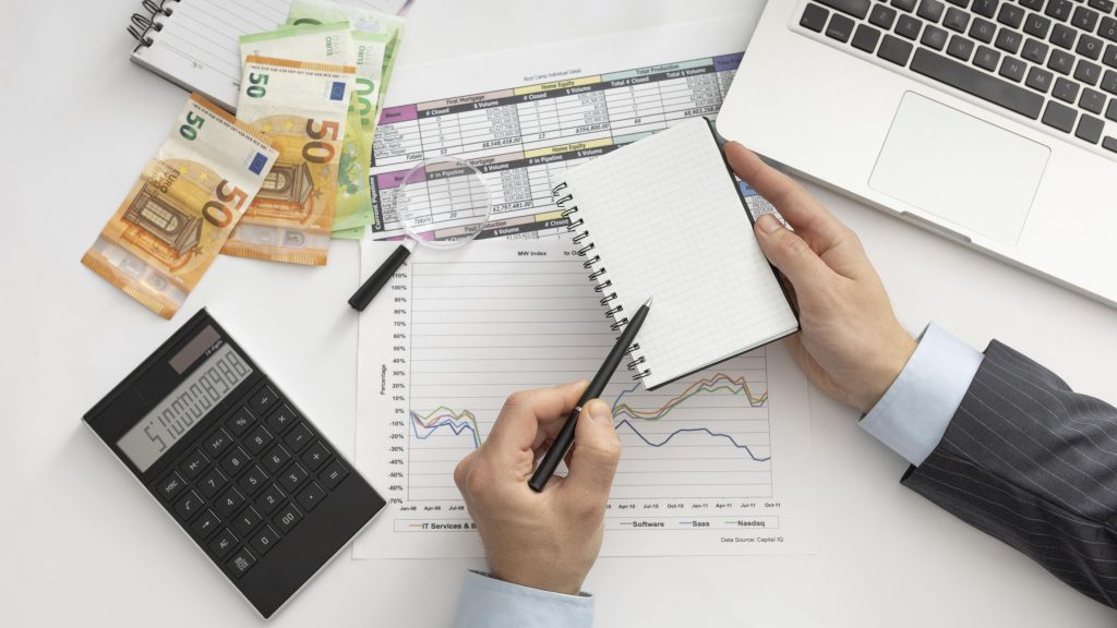 Büroarbeitsplatz mit Euro-Banknoten, Taschenrechner, Laptop und Finanzdiagrammen – ein Geschäftsmann plant Marketingstrategien und Investitionen für die Finanzbranche. Symbol für datengetriebenes Online-Marketing und digitale Performance-Analyse.