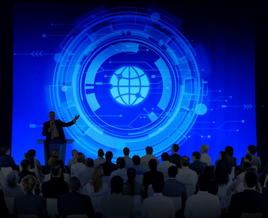 Speaker auf einer Digitalkonferenz spricht vor großem Publikum vor einer futuristischen Präsentation mit digitalem Globus-Interface – symbolisiert internationales Networking, Innovation und strategisches Digital-Marketing auf Fachmessen