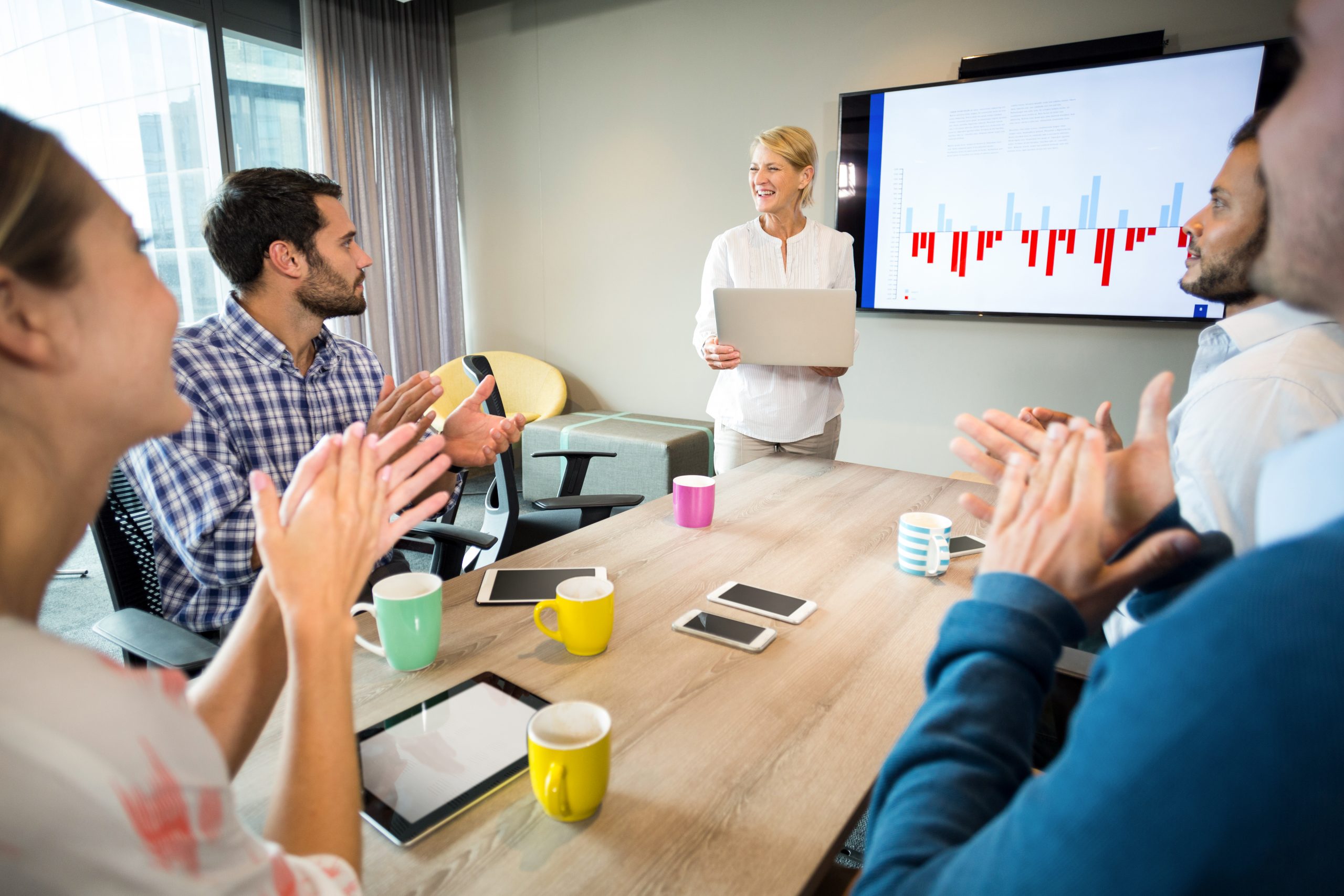 Personen in einem modernen Meetingraum bei einer Präsentation mit Balkendiagramm auf dem Bildschirm genau wie bei der SEO-Agentur komenci.